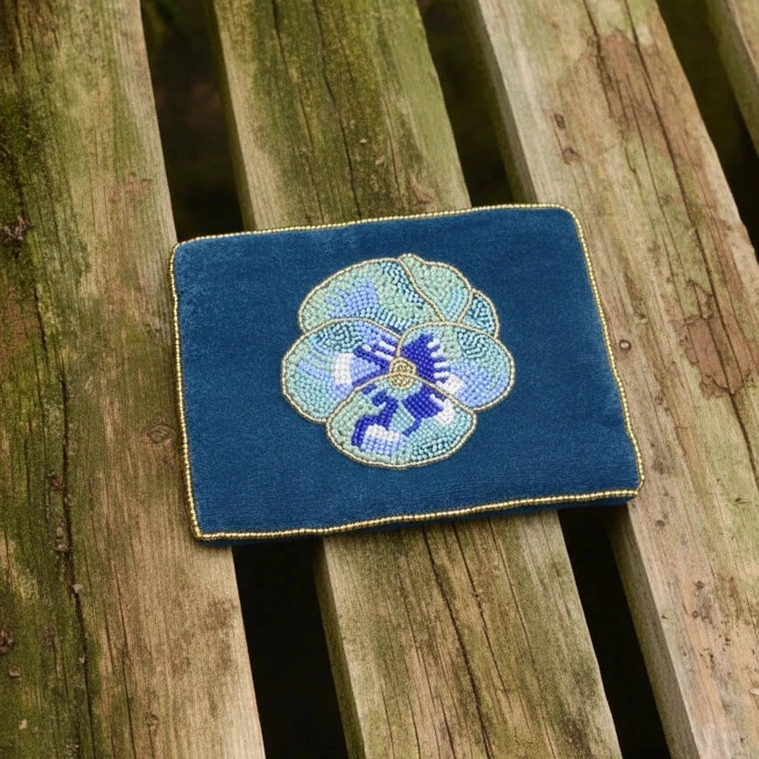 Two blue embroidered coasters with floral designs on a wooden surface with flowers.
