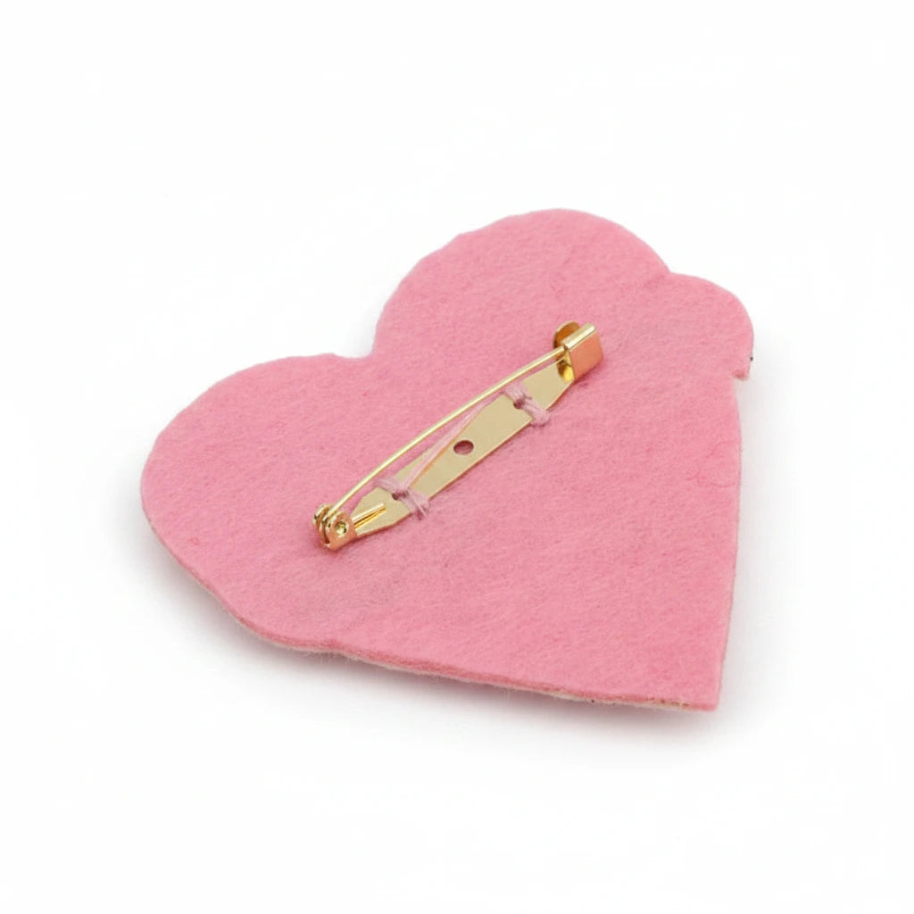 A pink felt heart-shaped pinback badge with a gold metal safety pin clasp, shown on a plain white background.