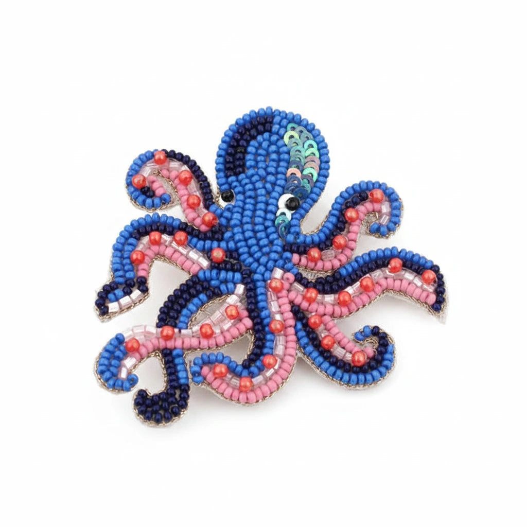A beaded octopus-shaped brooch featuring blue, pink, and red seed beads with small white bead eyes, displayed on a clean white background.