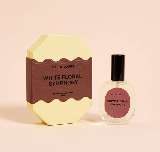 Celia Loves White Floral Symphony room and linen spray set, featuring a pale yellow octagonal box with a brown label next to a clear glass spray bottle with a black cap and matching label, on a warm beige background.